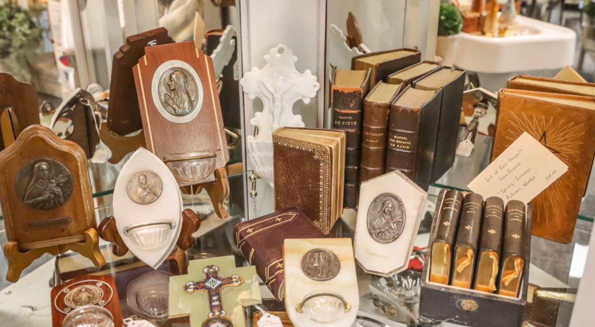 Glass case of antique books, religious medallions, and vintage curios.